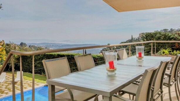 Un espace repas comprenant une table et des chaises, donnant sur une piscine et offrant une vue panoramique sur les montagnes.