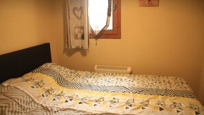 A bed with patterned bedding, a window with a heart-shaped decoration, and a wall-mounted heater.