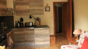 A compact kitchen with a built-in stove, a coffee maker, and a toaster. There is a wooden cabinet and a small table with a lamp.