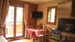 A cozy room with a dining table, chairs, a television, a small kitchen area, and a sliding glass door leading to an outdoor area.
