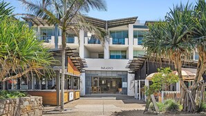 Un hôtel moderne doté d’une entrée centrale, de nombreux balcons et d’un aménagement paysager de style tropical.