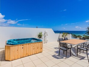 A wooden hot tub on a tiled patio with a table and chairs, overlooking a beach and ocean. - Luxury 3-bed oceanfront haven featuring a rooftop terrace with a private spa (Tweed)