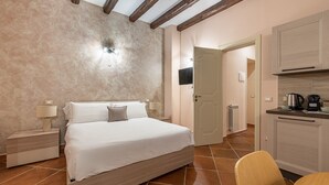 A bedroom with a bed, bedside tables, a nightstand, a wooden chair, a kitchen area with cabinets, a countertop, and a door leading to another room. - Casa agli Eremiti by Wonderful Italy (Palermo)