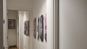 Ein Flur mit Holzboden und weißen Wänden. Mehrere Türen säumen den Flur, und ein Poster ist an der Wand zu sehen.
