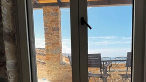 A room with a large window, a wooden ceiling, and a view of outdoor seating. - Tzia Stone Modern Studio with Sea View (Kea)