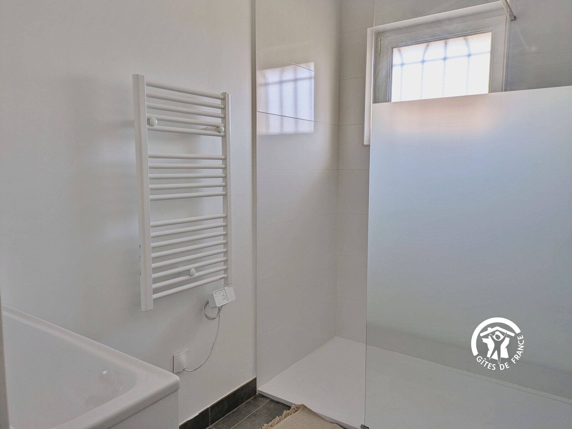 A bathroom with a white bathtub, a towel rack, and a window with blinds.