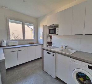 A modern kitchen with white cabinets, a built-in microwave, a sink, and a washing machine.