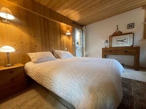 A wooden-paneled room with a bed, nightstands, a desk, and wall-mounted lamps.