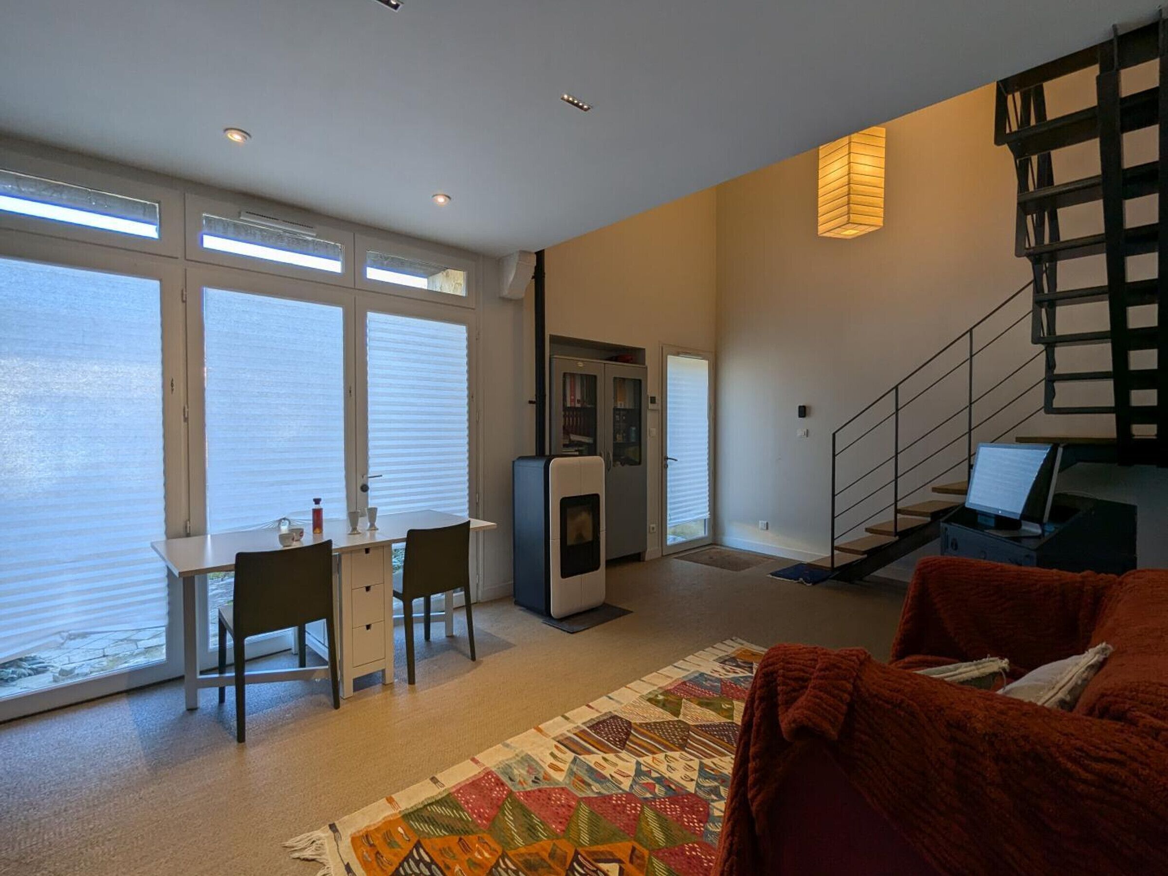 Een moderne woonkamer met een eethoek, een trap en uitzicht door grote ramen.