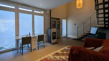 Een moderne woonkamer met een eethoek, een trap en uitzicht door grote ramen.