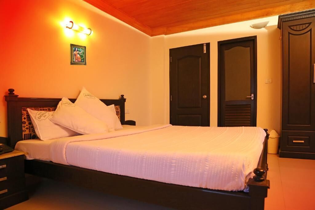 A neatly made bed with white bedding and pillows, a wooden headboard, and a wall-mounted light fixture.
