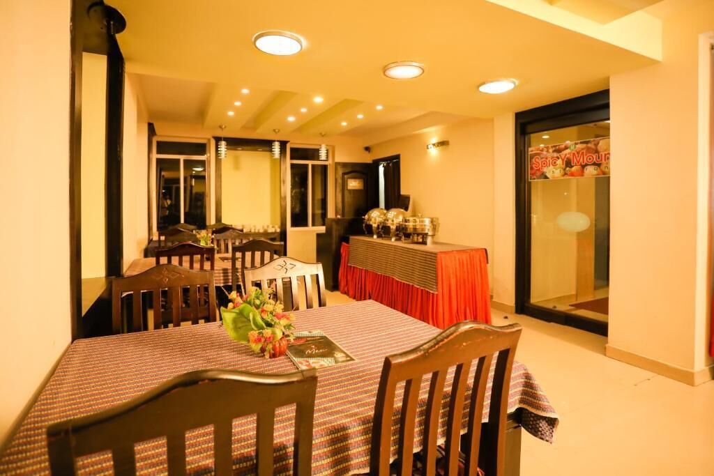 A dining area with a table set for four, surrounded by wooden chairs. There is a buffet table with a red cloth and a sign that reads "Spicy Moul".
