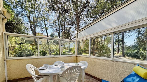 A sunroom with a table and chairs, large windows, and a view of trees. - Argelès T2 beach, park, parking, 4 pers (Argelès-sur-Mer)