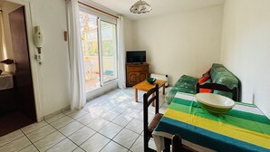 A compact living space with a dining area, a sofa, a television, and a sliding glass door leading to an outdoor area. - Argelès T2 beach, park, parking, 4 pers (Argelès-sur-Mer)