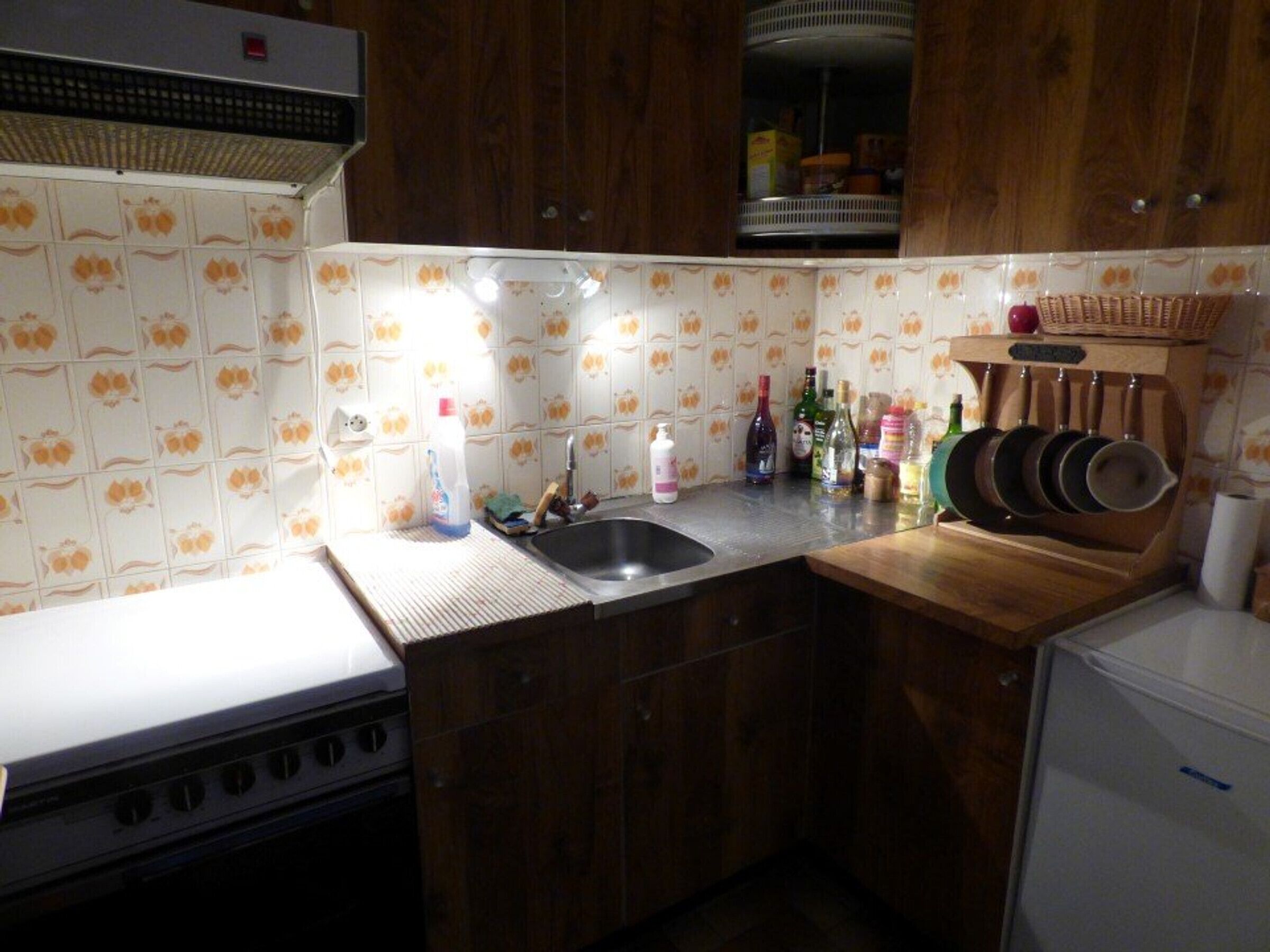 A kitchen with wooden cabinets, a stove, a sink, and various kitchen items on the countertop.