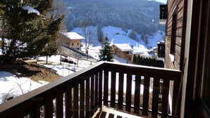 Un balcon en bois offrant une vue sur un paysage montagneux enneigé, avec des maisons et des arbres.