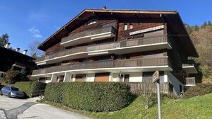 Un immeuble en bois à plusieurs étages, doté de balcons, d’une allée pavée et d’une haie bien entretenue.