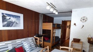 Une pièce de taille modeste, comprenant un lit superposé, un canapé avec des coussins à motifs, une table à manger et un tableau encadré accroché au mur.