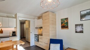 Eine kompakte Küche mit modernen Geräten, ein Essbereich mit Holztisch und einem blauen Stuhl.