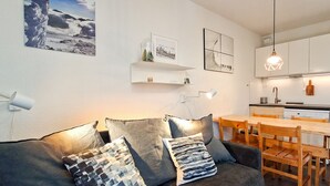 Ein modernes Wohnzimmer mit grauem Sofa, Esstisch aus Holz und Küchenbereich.