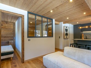 A modern interior with a wooden ceiling, a sofa, a dining area, and a view through a large window. - Premium apartment, 4 ppl, wifi (Val-d'Isère)