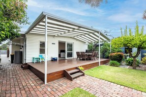 Eine überdachte Terrasse mit Holzboden, Gartenmöbeln und einem kleinen Gartenbereich.
