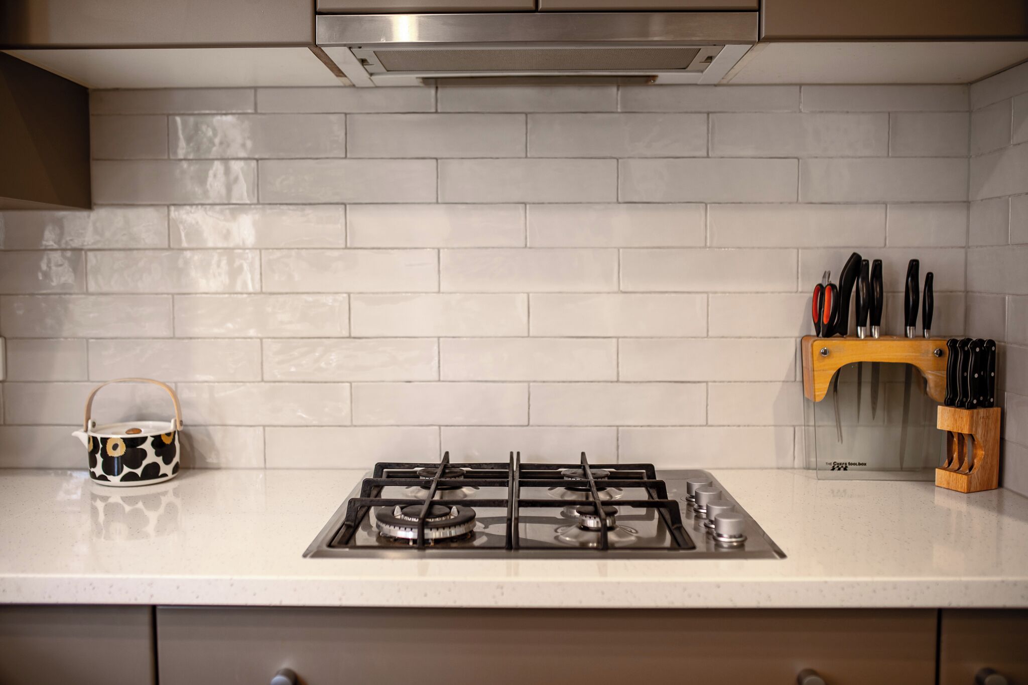 A kitchen with a gas stove, a kettle, and a knife block on the countertop.