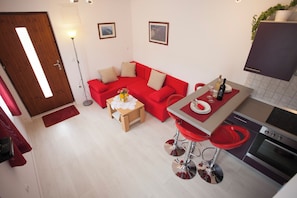 Un ambiente compatto con un divano rosso, un piccolo tavolo da pranzo, un angolo cottura con un piano cottura e uno sgabello da bar.