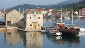 A stone building with a yellow door, surrounded by calm water and boats, with a mountainous backdrop. - Superior apartment in Stari Grad (Stari Grad)