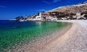 A coastal scene with clear turquoise waters, a pebble beach, and a stone building with a red-tiled roof. - Comfortable apartment in Stari Grad (Stari Grad)