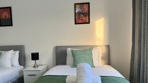 A hotel room with two beds, a nightstand, a lamp, and two framed pictures on the wall. - Edgbaston Birmingham Apartment (Birmingham)