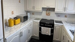 A kitchen with white cabinets, a black stove, a microwave, and two yellow kettles. - Edgbaston Birmingham Apartment (Birmingham)