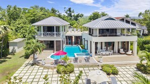 Ein zweistöckiges Haus mit Pool, Sitzgelegenheiten im Freien und üppiger Bepflanzung.