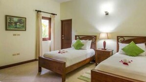 A hotel room with two wooden beds, a wooden wardrobe, a small bedside table with a lamp, and a framed picture on the wall. - Hospitality Expert - Little Waters Villa Negril (Negril)