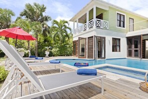 Ein zweistöckiges Haus mit Swimmingpool, Holzterrasse und Liegestühlen.