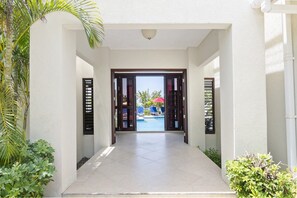 A hotel entrance with a pool view, a covered seating area, and a security camera above the door. - Hospitality Expert - Little Waters Villa Negril (Negril)