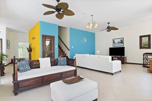 A living room with a sofa, a coffee table, a TV, and a staircase. - Hospitality Expert - Little Waters Villa Negril (Negril)