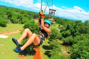 A person zip-lining through a forested area with a clear sky.