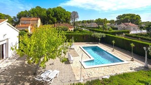 Une piscine dotée d’une plage en pierre, entourée d’un jardin bien entretenu et d’un bâtiment blanc.