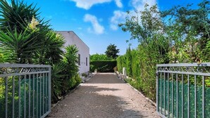 Un chemin de gravier mène à un bâtiment blanc, de chaque côté duquel se trouve un portail en métal.