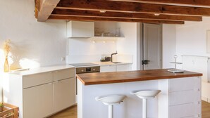 A modern kitchen with white cabinetry, a wooden countertop, and two white bar stools. - Rue du Centre | Bright duplex near Montreux train station (Montreux)