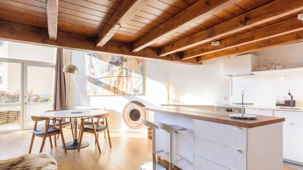 A modern kitchen with wooden beams, a central island, and a dining area with a round table and chairs. - Rue du Centre | Bright duplex near Montreux train station (Montreux)