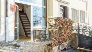 A residential building with a staircase leading to an upper floor, a small outdoor seating area with a table and chairs, and a potted plant. - Rue du Centre | Bright duplex near Montreux train station (Montreux)