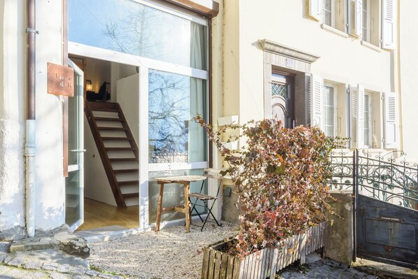 Un edificio residencial con una escalera que lleva a un piso superior, un pequeño espacio al aire libre con una mesa y sillas, y una planta en maceta.