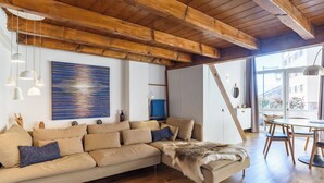 A modern living room with a wooden ceiling, a large abstract painting, a sofa with cushions, and a dining area with a table and chairs. - Rue du Centre | Bright duplex near Montreux train station (Montreux)