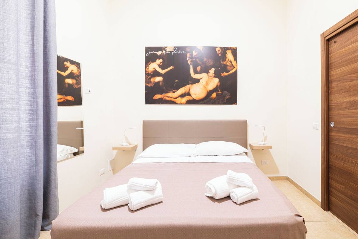 A hotel room with a bed, two white towels, a wooden door, and a painting on the wall.