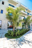 A modern building with a stone facade, multiple balconies, and a landscaped courtyard with palm trees and shrubs.