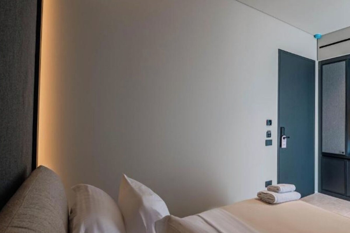 A modern hotel room with a neatly made bed, a sofa, and a door leading to a bathroom.