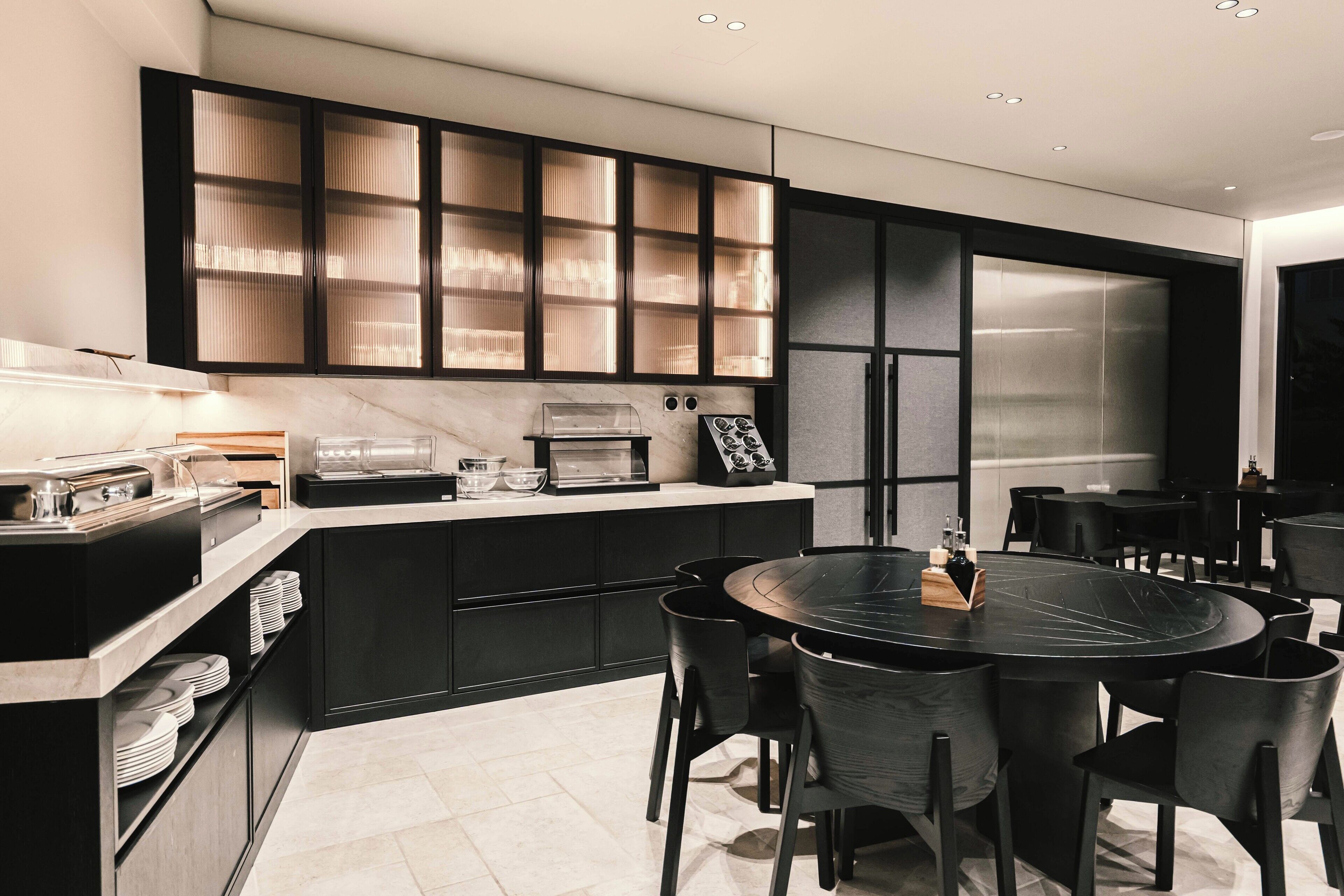 A modern kitchen with black cabinets, a marble countertop, and a round dining table with chairs.