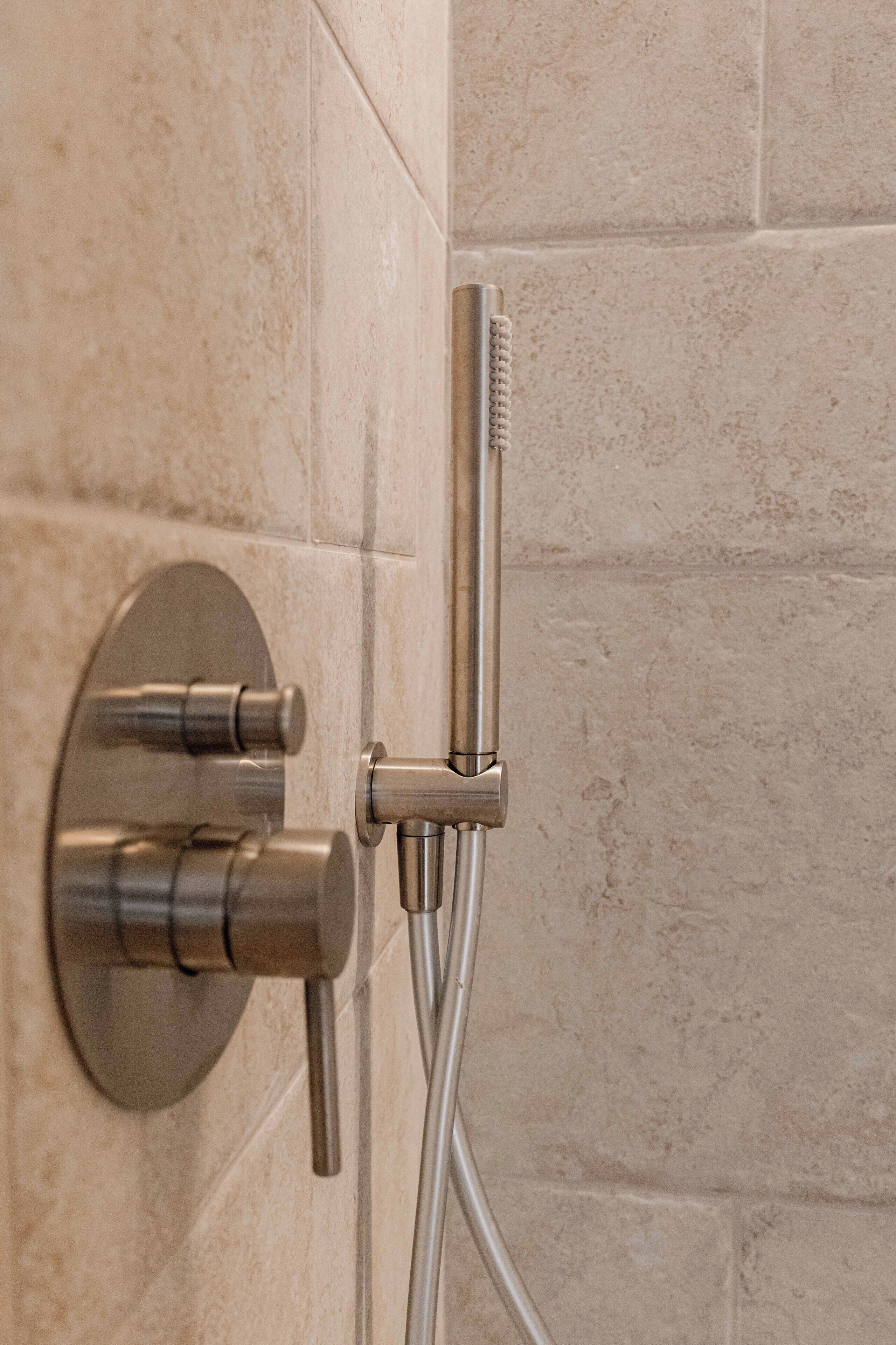 A modern shower with a handheld showerhead and a wall-mounted control valve.